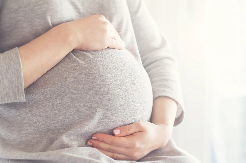 Ein Schwangerschaftsbauch, der oben und unten von den Händen der Schwangeren eingerahmt wird.