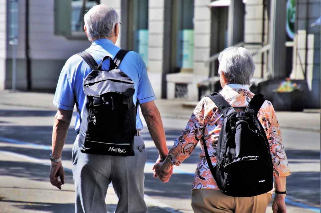 Ein älterer Herr und eine ältere Dame von hinten, die Hand in Hand auf der Straße gehen
